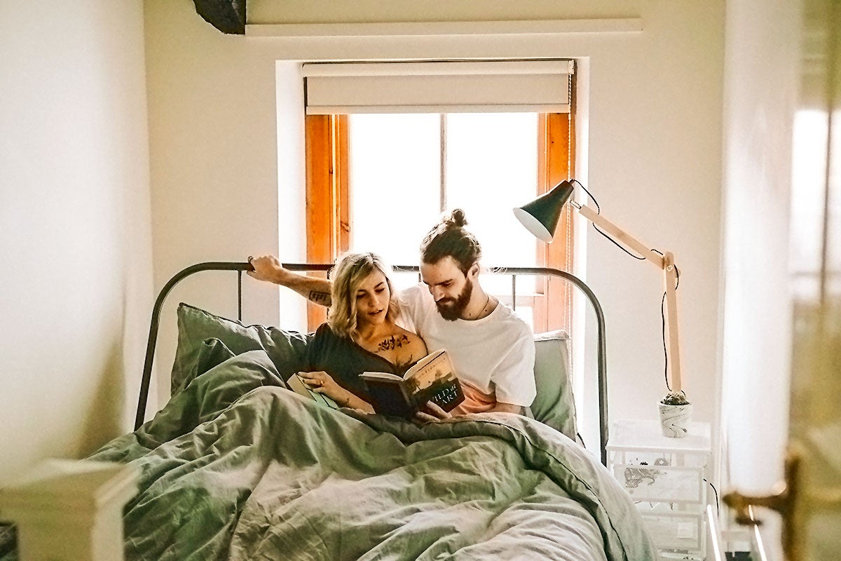 A couple reads a book together in bed as part of a romantic stay-at-home date night