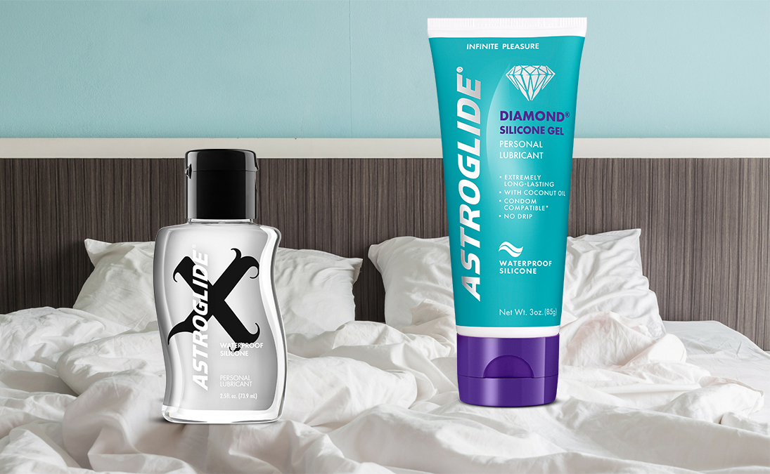 Two bottles of ASTROGLIDE silicone lubricant standing on a bed