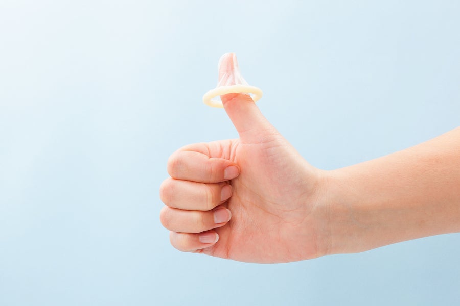 A hand gives the thumbs up with an unrolled latex condom on the thumb