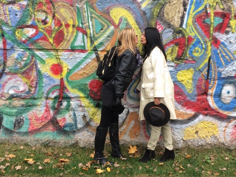 picture of lesbian couple kissing in front of a mural. One woman is wearing all black, and one all white.